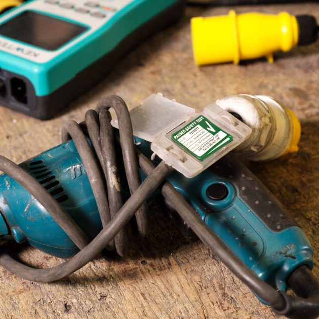 A power tool with a coiled cable and a plug on a wooden surface with other tools.
